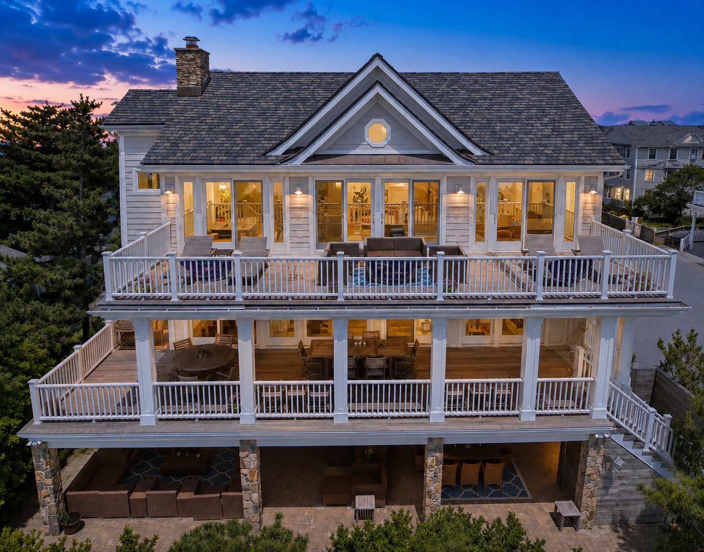 Twilight rear exterior photograph of a multi-level coastal home with illuminated decks in Long Beach, New York